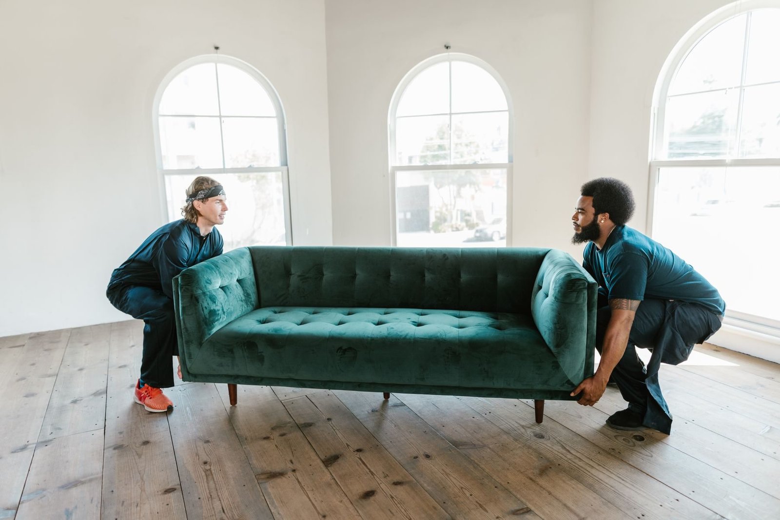 Two workers carrying a green sofa inside a home